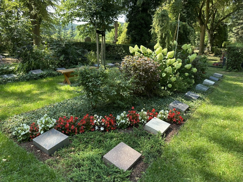 Gehölzgarten mit Sträuchern und kleinen Bäumen; geschützter, geborgener Ort der Erinnerung.